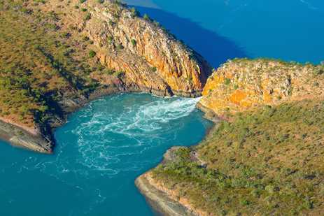 Two land masses almost touching above water, letting a stream of azure sea flow into a small blue-green bay